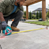Landscape installer using a Total fibreglass tape to measure pergola footing spacing on a residential slab
