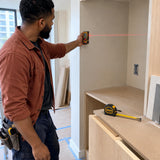 African American cabinet installer using the Ingco laser distance detector and steel tape to measure a recessed shelving alcove.