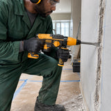 African American renovation installer using an Ingco CRHLI26208 rotary hammer to chisel a narrow masonry service chase.