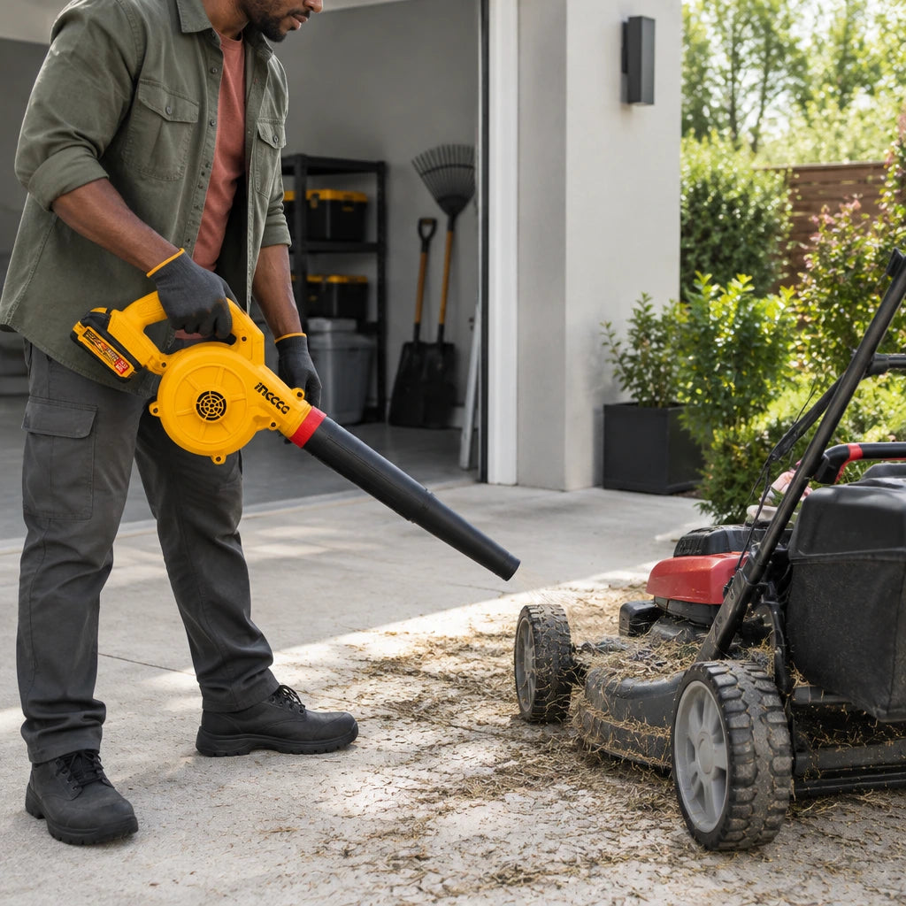African American home-maintenance user directs the Ingco CABLI20782 cordless blower across dry clippings on a lawn mower.