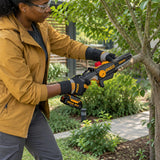 African American home gardener using an Ingco 20V cordless pruning saw to cut a selected branch from an ornamental garden tree.