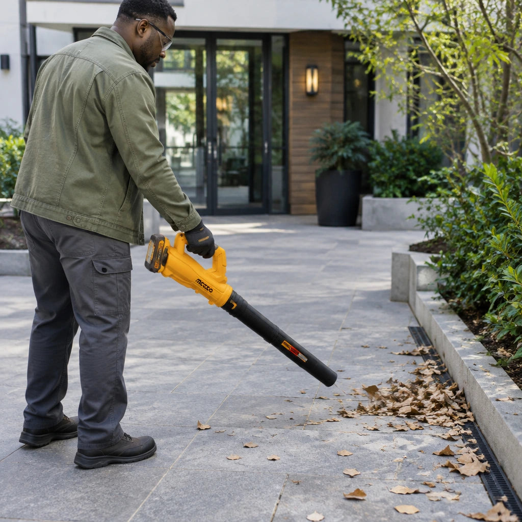 Facilities worker using the Ingco CABLI203232 cordless blower to clear dry leaves from a paved courtyard entrance