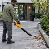Facilities worker using the Ingco CABLI203232 cordless blower to clear dry leaves from a paved courtyard entrance