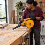 African American woodworker uses the Ingco AB6508 variable-speed blower to clear sawdust from a tabletop in a home workshop.