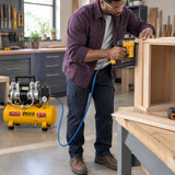 African American joiner using a pneumatic brad nailer connected to the Ingco ACS111062 compressor to secure cabinet trim