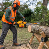 African American groundskeeper using an Ingco 20-inch gasoline chainsaw to cut a supported timber log outdoors