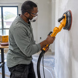 African American drywall finisher using a compatible sander with an Ingco 180mm hook-and-loop disc on a skim-coated wall