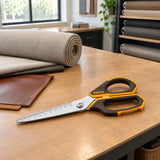 Ingco construction scissors resting on an upholstery cutting table beside fabric and leather samples