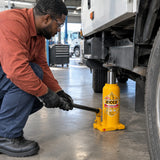 African American fleet technician operating an Ingco HBJ1002 bottle jack beneath a compatible vehicle in a clean service bay.