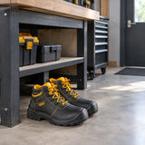 Ingco black steel-toe safety boots resting beneath a bench in an organised professional workshop entrance.