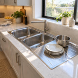 Clean Reginox double-bowl kitchen sink with rinsed dishes draining on the integrated right-hand drainer