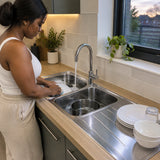 Adult washing dishes in a Reginox double-bowl kitchen sink with items draining on the right