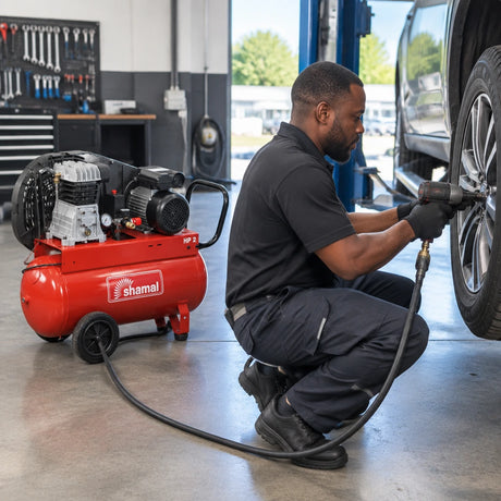 African American automotive technician using a pneumatic impact wrench connected to a Shamal air compressor at a workshop wheel