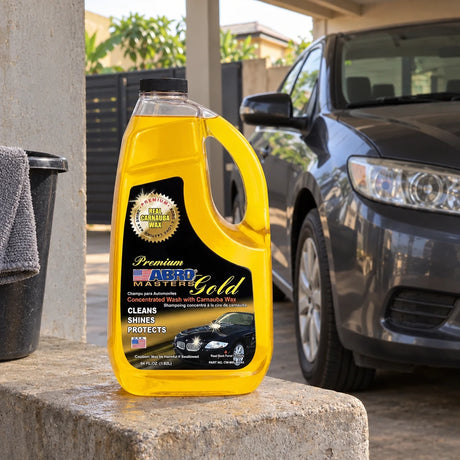 Abro Premium Gold Car Wash bottle resting on a concrete ledge beside a parked car in a Ghanaian carport