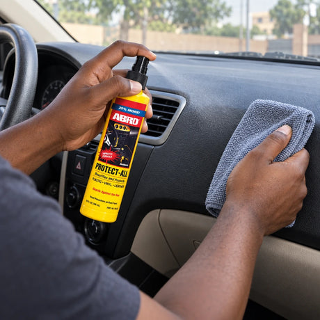Person using Abro PA-512-AM dashboard cleaner to apply spray to a microfiber cloth inside a car