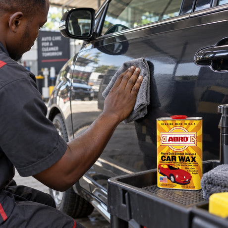 Ghanaian detailer buffing a car panel with a cloth beside an open Abro SW-300 car wax tin