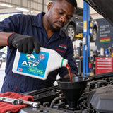 Technician pours Abro Premium Dexron III Mercon ATF from a 1 litre bottle into a vehicle transmission service point