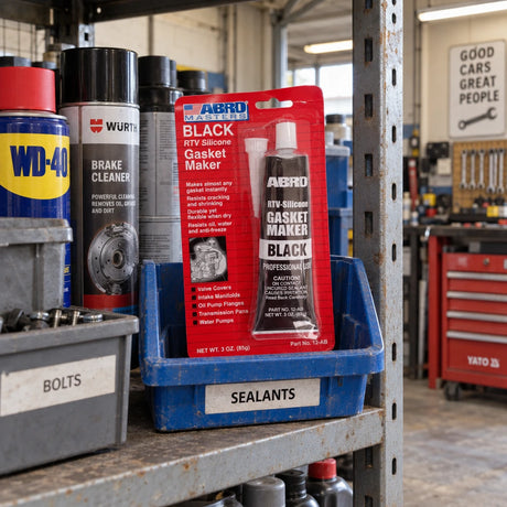 Unopened Abro Black RTV Silicone Gasket Maker stored in a parts bin on an automotive workshop shelf.