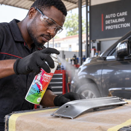 Ghanaian automotive technician using an Abro spray paint can to refinish a prepared metal trim panel