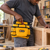 Ghanaian carpenter retrieving a hand tool from a Coofix yellow waist tool bag while assembling a timber cabinet