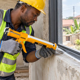 Ghanaian tradesperson applying sealant with a Coofix cartridge caulking gun along a window frame