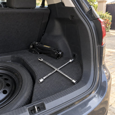 Coofix four-way cross rim wrench resting in a vehicle boot beside the spare wheel