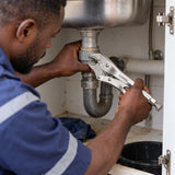 Ghanaian maintenance worker using Coofix curved-jaw locking pliers on a rounded plumbing fitting beneath a sink