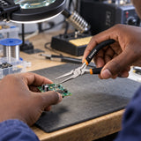 Ghanaian electronics technician using Coofix mini needle-nose pliers to position a small wire on a circuit board
