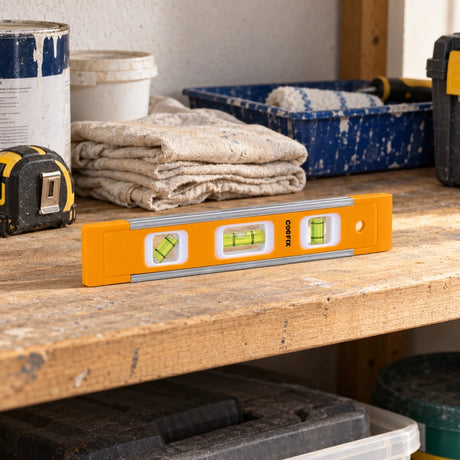 Coofix orange mini spirit level resting on a wooden workshop shelf among decorating tools