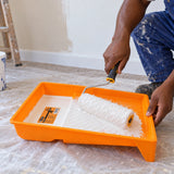 Ghanaian decorator loading a paint roller with white paint in a Coofix orange paint tray