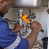 Ghanaian plumber using a Coofix orange and black pipe wrench to tighten a threaded pipe fitting under a sink
