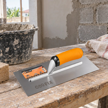 Coofix stainless-steel plastering trowel resting on a mason’s workbench at a wall renovation site