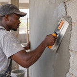 Ghanaian plasterer using a Coofix stainless-steel trowel to smooth fresh wall plaster