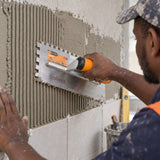 Ghanaian tiler using a Coofix toothed stainless-steel trowel to form adhesive ridges on a wall
