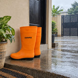Orange Coofix rain boots standing by a damp concrete entrance before outdoor work