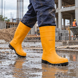 Ghanaian construction worker wearing yellow Coofix rubber safety boots while walking across a wet concrete worksite