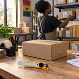 Completed parcel on a Ghanaian packing bench with a Coofix snap-off blade knife ready beside it