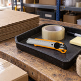 Coofix snap-off blade knife resting in a tool tray on a packaging workstation beside cartons