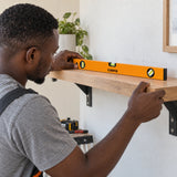 Ghanaian tradesperson using a Coofix orange spirit level to check a timber wall shelf during installation